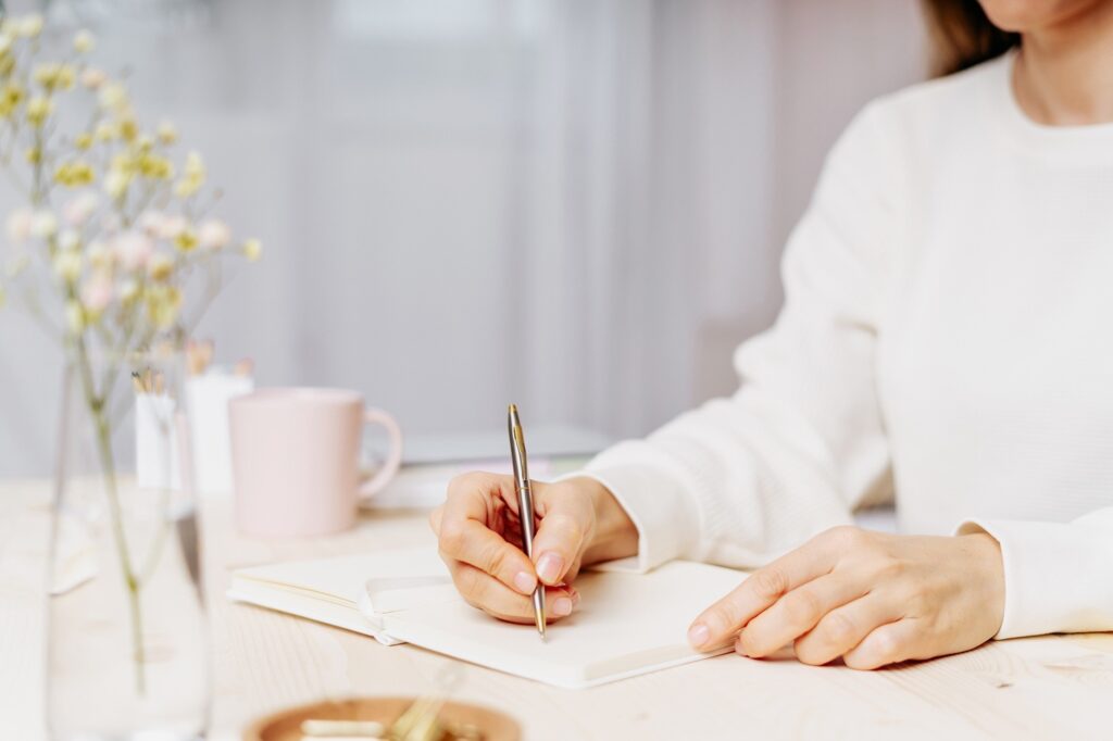 Woman Writing In Notebook At Desk At Home